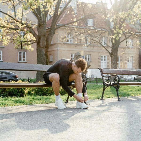 A smiling middle-aged man tying his running shoes in a sunlit park, ready for activity.